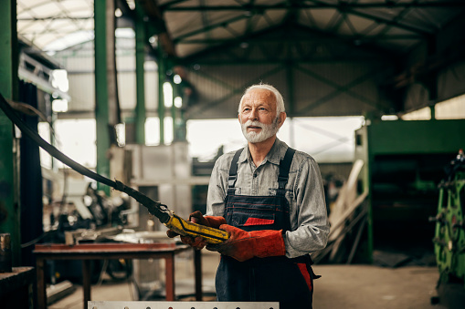 A senior heavy industry worker is operating machines in factory.